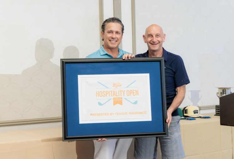 Two smiling men holding a framed "Hospitality Open" event sign at the San Diego Tourism Authority Golf Tournament
